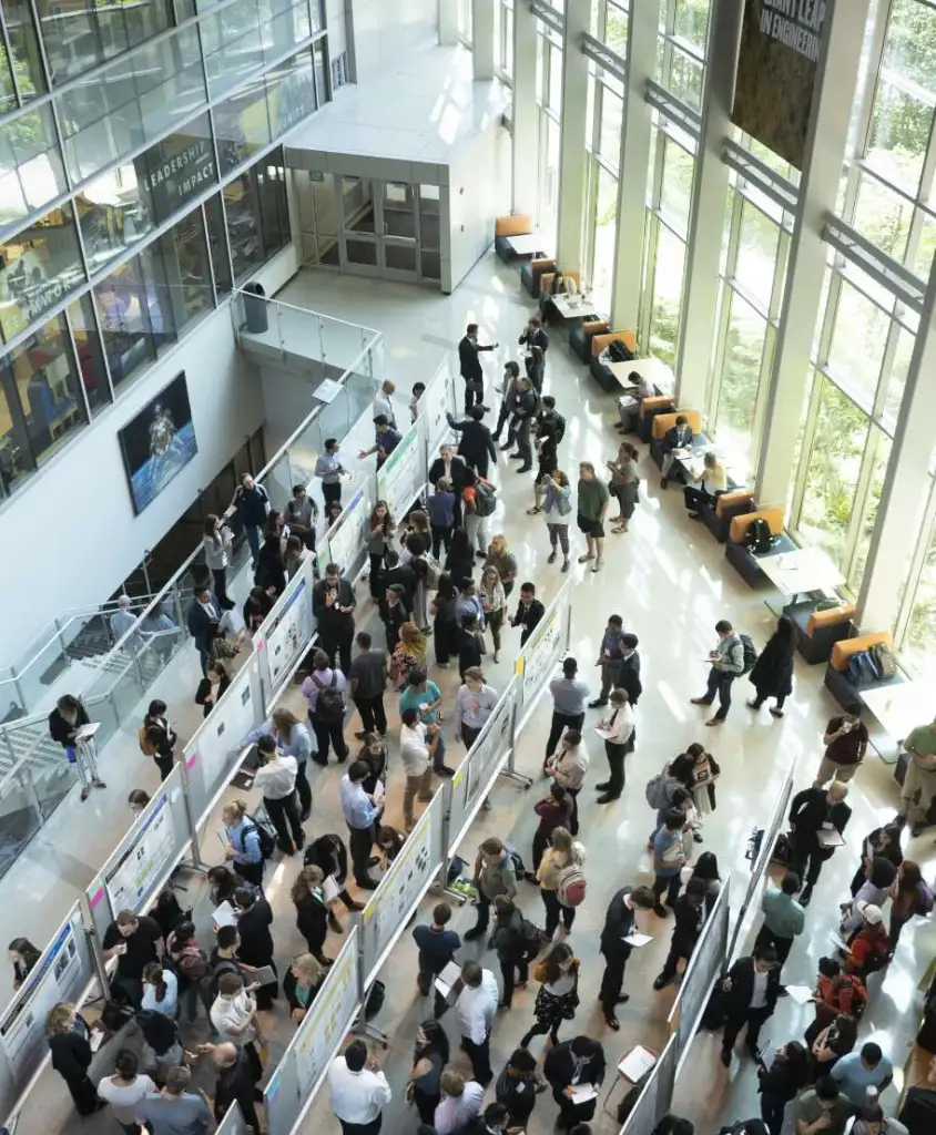 Taken from a high balcony, an overhead shot of a large group of people circulating among research posters - Discovery Park District at Purdue - Purdue Research Foundation