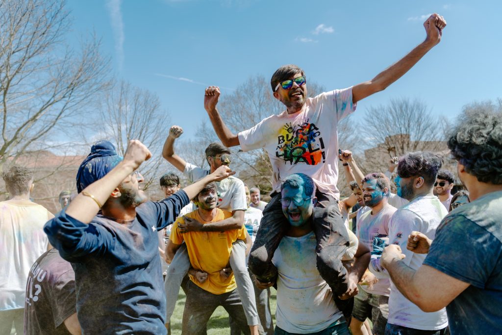 A group of Purdue students, some sitting on the shoulders of others, celebrate Holi and are covered in multicolored powder - Discovery Park District - Purdue Research Foundation