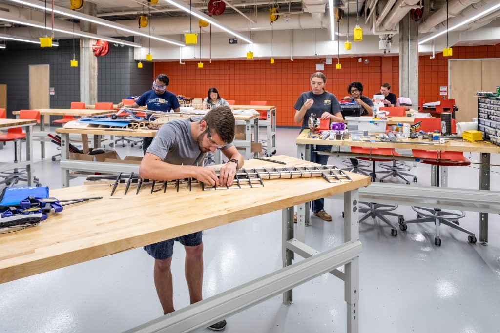 6 students work on various engineering projects at separate desks in a bright and cheerful space - Discovery Park District at Purdue - Purdue Research Foundation