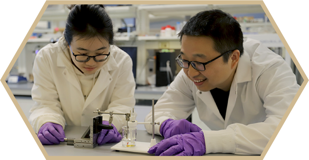 Two researchers in lab coats lean over scientific equipment in a lab setting - Discovery Park District at Purdue - Purdue Research Foundation